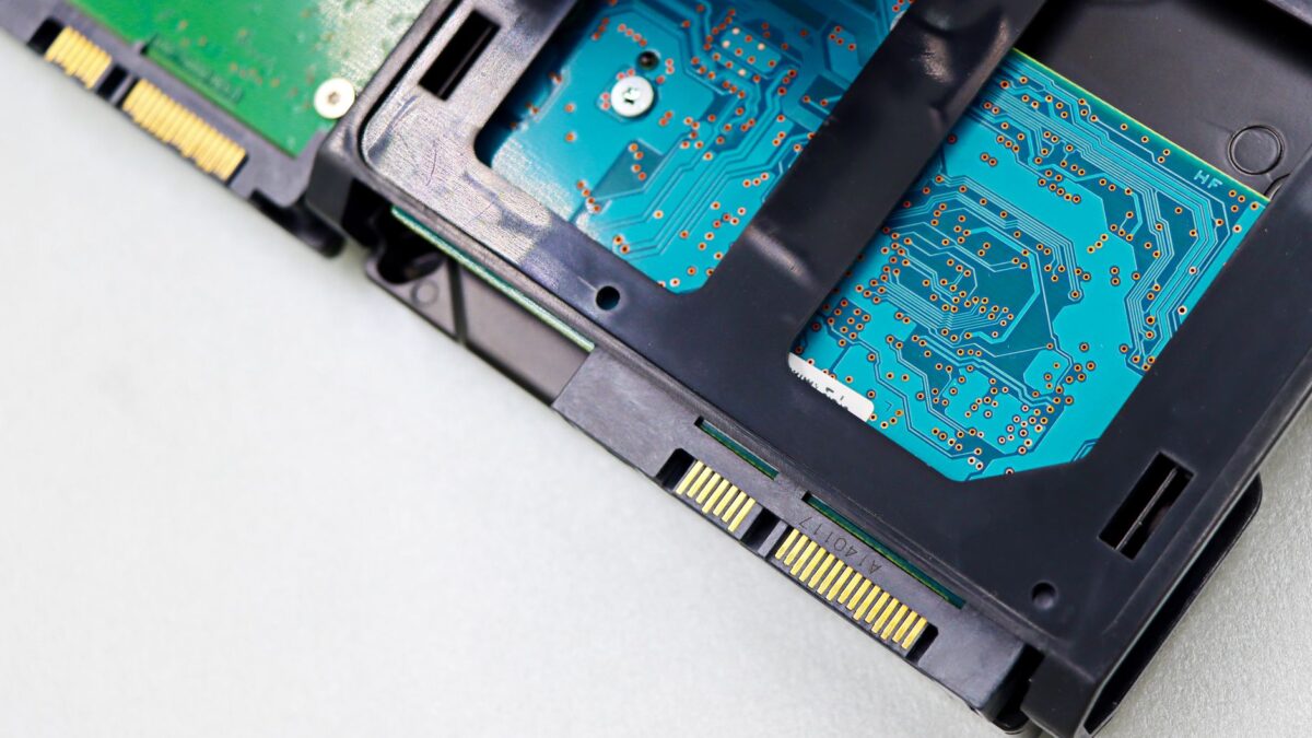 Gros plan sur un disque dur ou SSD démonté : circuits imprimés bleus et verts, connecteurs SATA dorés, boîtier noir en plastique, fond blanc neutre.