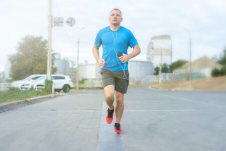 Adult man jogging on a road, wearing earphones and carrying a smartphone, embracing an active lifestyle.
