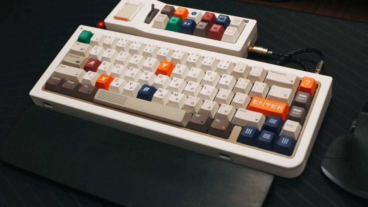 Clavier mécanique compact au style rétro, touches beige, marron, orange et bleu marine, inscriptions japonaises, posé sur un tapis de souris noir, avec un câble tressé noir.