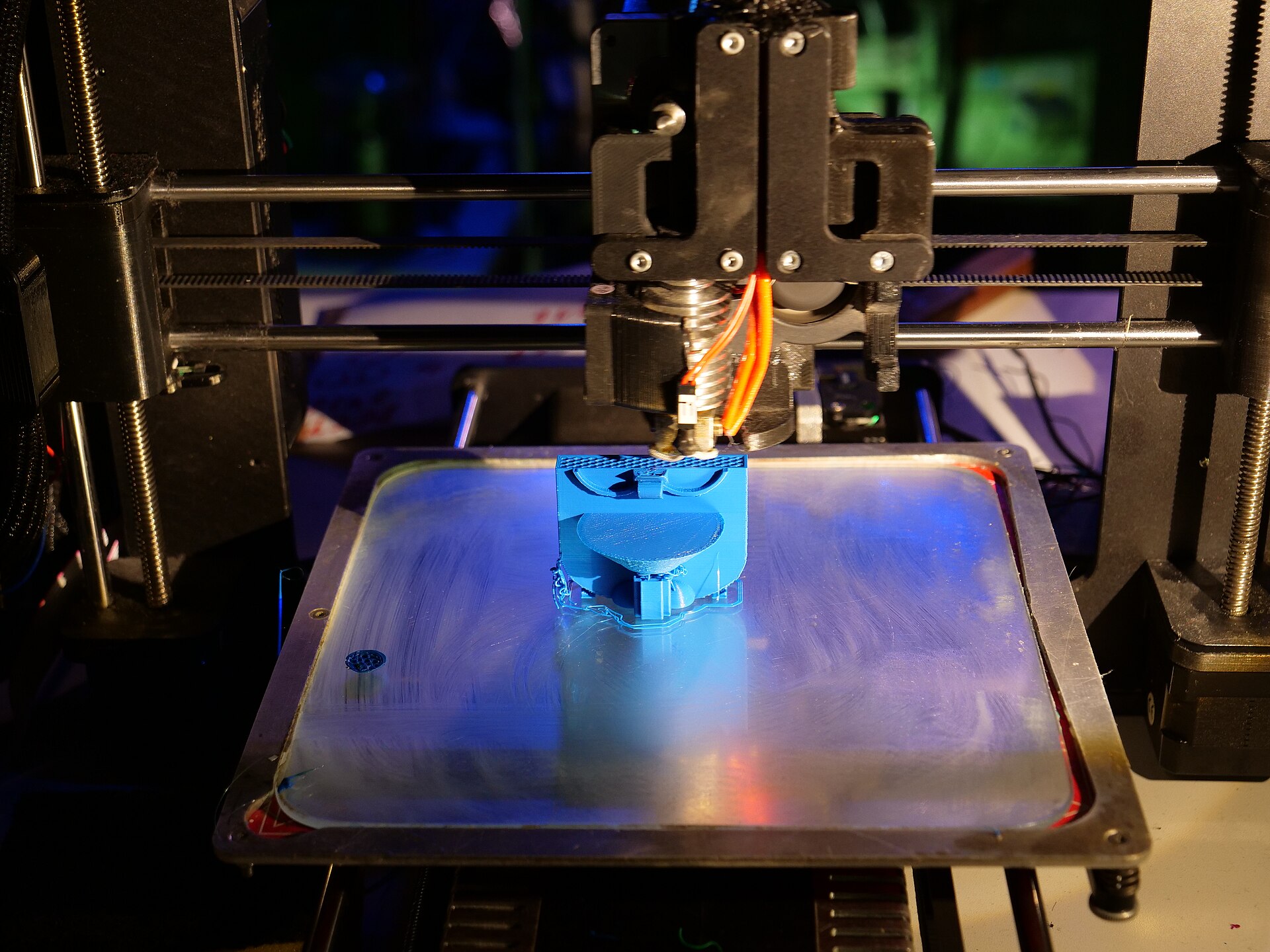 Close view of a desktop 3D printer laying down a blue plastic part on its heated build plate